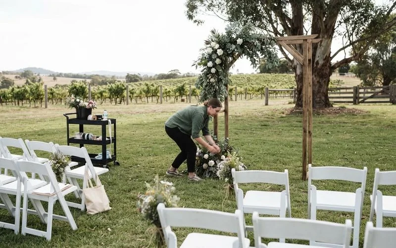 An outdoor wedding ceremony setup with white chairs facing an arbour among vines at a Swan Valley winery